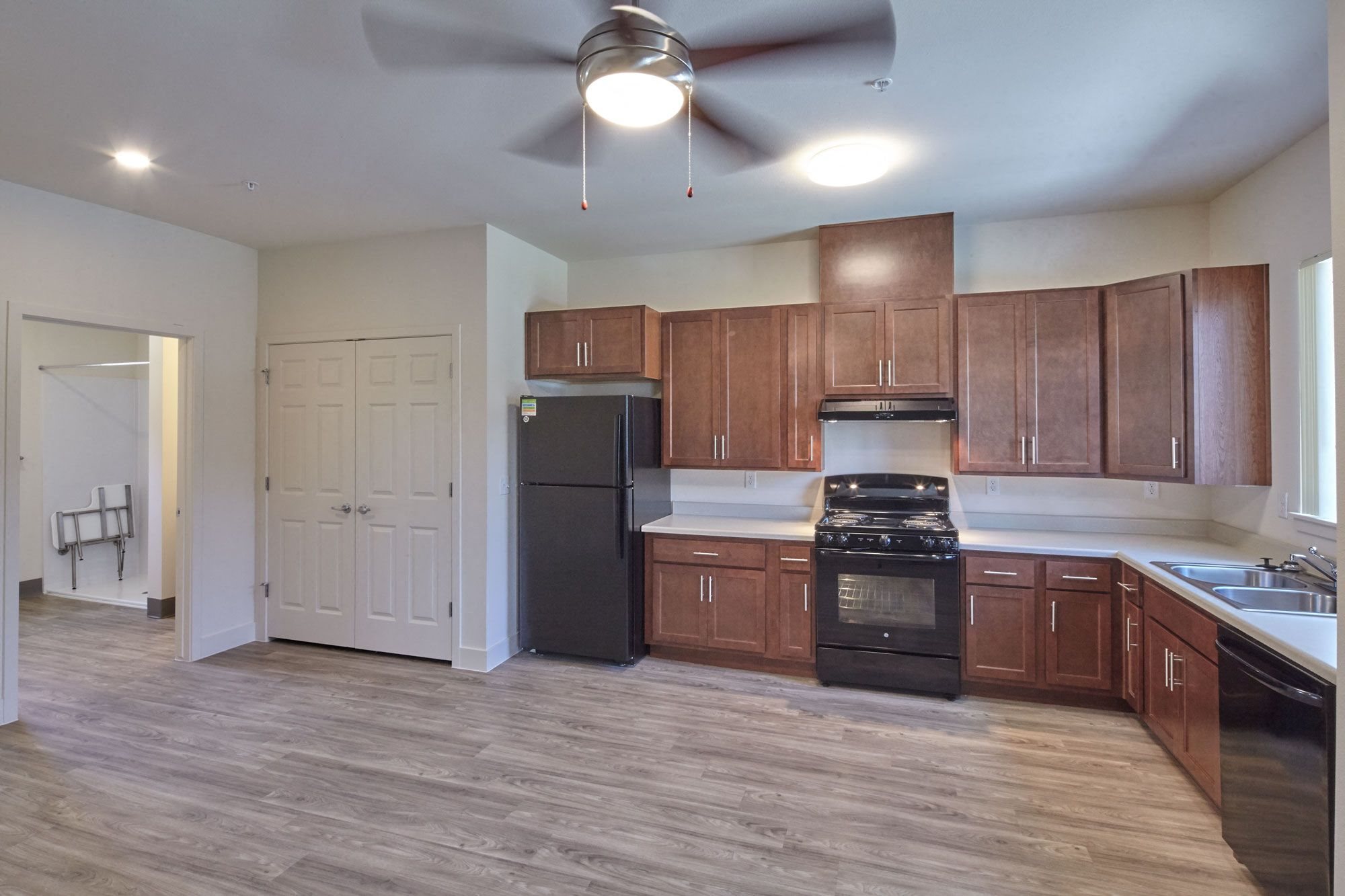 Open concept kitchen with brown cabinets, light grey counters, sink, dishwasher, refrigerator, stove and vent hood